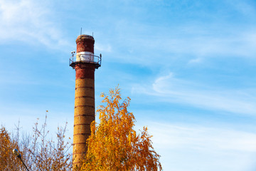 Old brick pipe of a thermal power plant near an autumn tree on a background of a beautiful sky with feather clouds