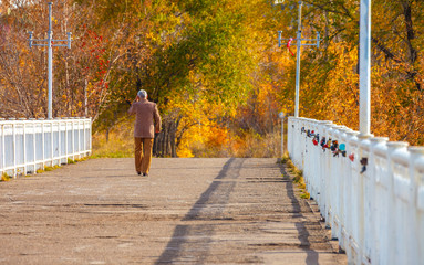 A man goes into the distance on a bridge with a white fence in an autumn park on a warm sunny day