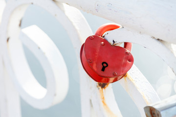 Red heart-shaped lock denoting love hanging on a white fence