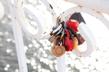 Many heart-shaped locks hang fastened on a white fence on a background of shiny water