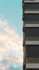 A modern multistory building against a dramatic, evening sky with Cumulus clouds illuminated by the sun against a blue sky. Residential building with air conditioning fans. Vertical photo. 