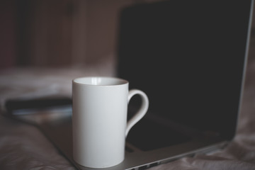 Obraz na płótnie Canvas White cup of tea on laptop in bed close up. Quarantine time. Good morning. Brekafast.