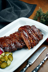 Close up view on tasty delicious bbq coocked ribs with barbecue sauce in white plate on wooden background. Classical american Barbecued Pork in composition with ingridients