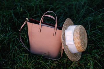 women handbag and boater with white ribbon on green grass.