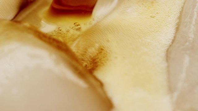 Macro brown soda pours over ice cube and carbonation fills the glass