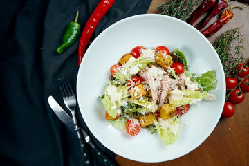 Caesar salad with croutons, parmesan, chicken, egg in black plate on colored background. Restaurant serving. Close up
