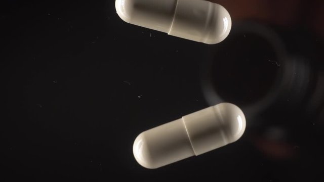 The white capsules fall out of the glass jar.Black background,slow motion,macro