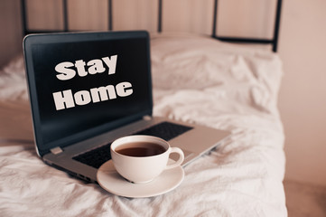 Cup of coffee on laptop with stay home text in bed closeup. Good morning. Breakfast time.