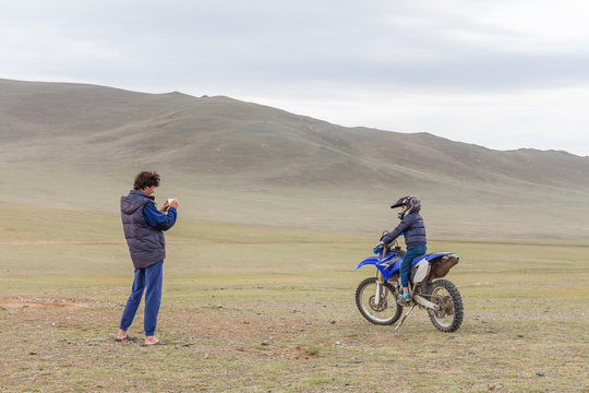 Father takes pictures of the happy son. Boy sitting in a helmet on a motorcycle in Mongolian Altai