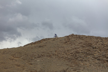A lone motorcyclist on top of a mountain against a dark sky before a storm. Mongolia, Altai.