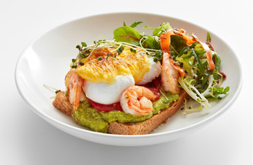 eggs benedict with hollandaise, shrimps and guacamole on toast with salad
