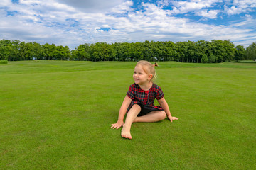 Fototapeta premium Cute little girl in dress on grass at green park. Summer portrait of baby 3 tree years old