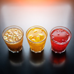 Three hot drinks of frozen berries and fruit on a black table in the sunlight.