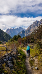 A girl with a big blue backpack hikes along a pathway on Annapurna Circuit Trek in Himalayas, Nepal. There are mountain chains around her. In the back there is a massive barren mountain range