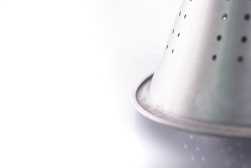 Shiny stainless steel metallic detail strainer isolated in a white minimalist kitchen.