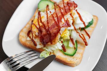 A bacon and egg sandwich on a white plate with a fork and knife. Close up.