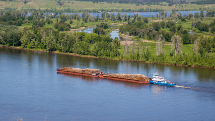 pusher vessel pushing two barges with logs along the Kama River, view from the high bank
