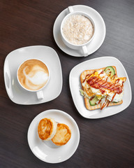 Breakfast consists of oatmeal porridge with cheesecakes and cappuccino with sandwich, top view.