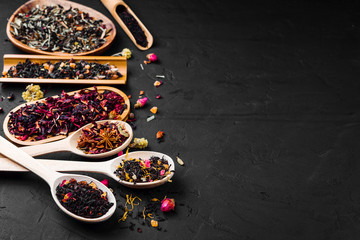Set of different herbal and fruit tea.Assorted dried tea leaves in wooden spoons on a concrete black background. Dark moody.
