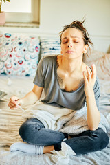 Sick woman with thermometer sitting in bed with cold and high fever.