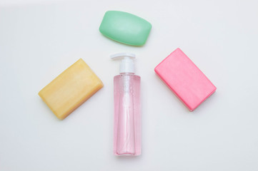 Three pieces of soap of different colors antibacterial, household and perfume next to a bottle of gel with a dispenser on a white background view from the top