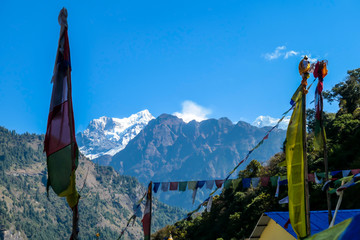 Colorful prayer flags waving above the Himalayan peaks along Annapurna Circuit Trek, Nepal. Meditation and peace of mind. High, snow caped mountains peaks catching the first beams of sunlight