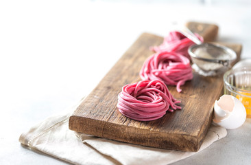 Fresh Hand made beetroot pasta on wooden cutting board. Raw purple spaghetti, fettuccine.