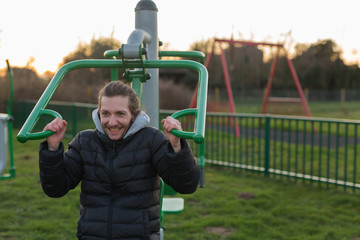 A young adult male using public exercise equipment in his local