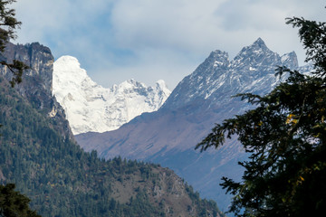 Fototapeta premium View on Himalayas, Annapurna Circuit Trek, Nepal. The view is disturbed by dense tree crowns in the front. High snow caped mountains peaks catching the first beams of sunlight. Serenity and calmness
