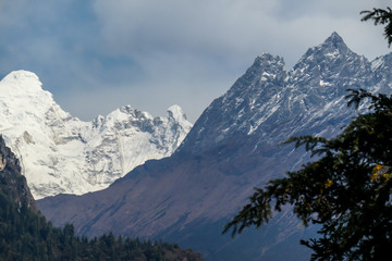 View on Himalayas, Annapurna Circuit Trek, Nepal. The view is disturbed by dense tree crowns in the front. High snow caped mountains peaks catching the first beams of sunlight. Serenity and calmness