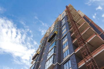 Facade work with construction cradle. Wall decoration of a building under construction with construction cradle