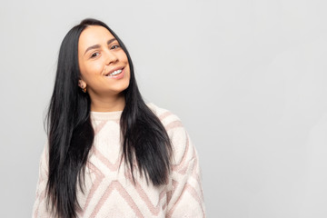 Obraz premium Portrait of a smiling Young beautiful lovely brunette girl in a warm winter sweater on light gray background.