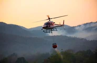 Fototapete Hubschrauber Der Helikopter schöpft Wasser aus dem Stausee und wird bewässert, um den brennenden Wald in den Bergen zu löschen.