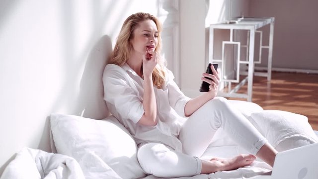 Woman stays in bed paints lips using a telephone instead of a mirror