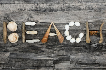 Abstract of seashells, driftwood and pebbles forming the word beach on rustic wood background. Holiday concept background.