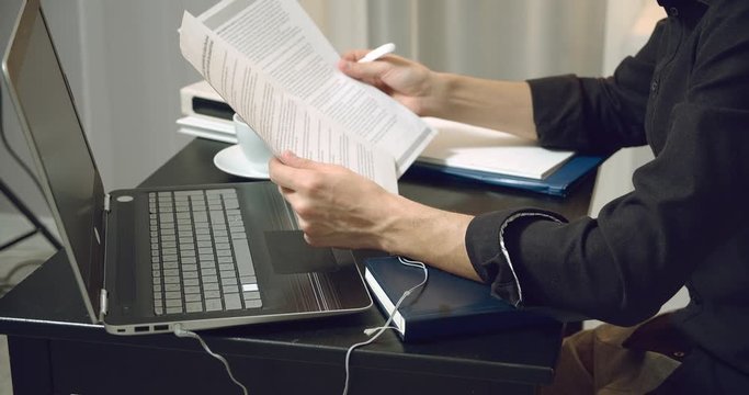 Close-up of male hands holding papers and making notes in the contract sitting at the table. Male entrepreneur reading documents, analyzing financial papers, preparing audit report at workplace