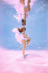Woman under water is stylishly dressed in glasses and a cup.