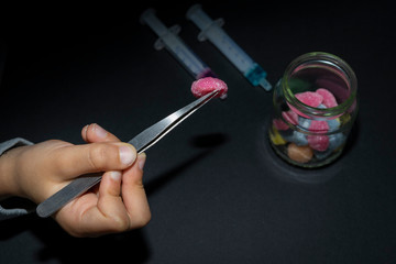 Close up hands of a child using metal tweezers to pick up colored jelly bean injected with liquid