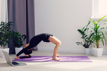 alone girl doing yoga exercises online on laptop on the floor in the light room, stay home safe...