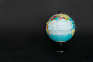 Earth globe dressed in a protective mask on the hands of a man in protective gloves. Symbol that people all over planet are quarantined due to epidemic and pandemic of Coronavirus. Black background.