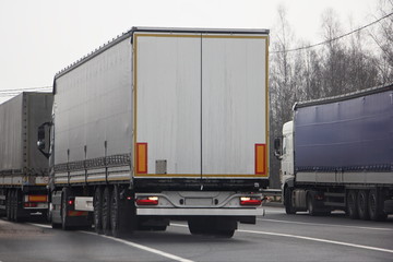 A lot van trucks queue on asphalt road near control point rear view at spring day, transit cargo shipping