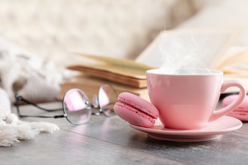 Cozy home composition. Book, plaid, steaming cup coffee or hot drink and macaroon on wooden white table. Front view, copy space
