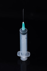 A medical syringe with a needle stands on a white table on a black background. photo for design or advertising