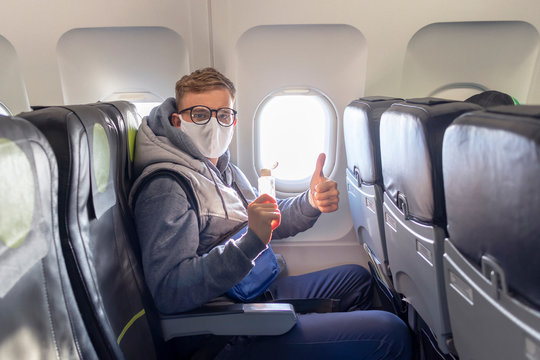  man on airplane show thumb up in glasses, medical protective sterile mask on his face sitting on plane using, apply anitizer for disinfect hands against coronavirus, virus bacteria. Pandemic covid-19