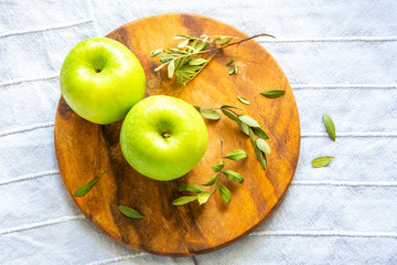 Green apples on the wooden tray on the table cloth