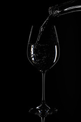 Silhouette of a wine glass, water is poured from a bottle, against a black background with reflection in Zurich, Europe, Switzerland.