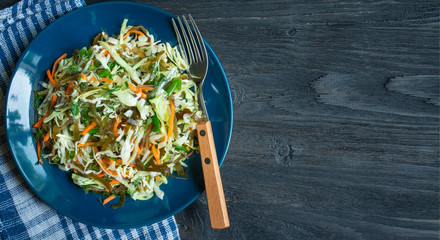 Salad of white cabbage, seaweed, carrots and herbs in a plate on a wooden table. A fresh vegetable salad. Food background. Vegetarian dish. View from above. Copy space. © Юлия Ромашко