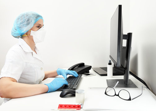 A doctor in a mask and gloves works on a computer in a polyclinic, a hospital in an emergency room.Doctor woman at work. reception desk at clinic or.Portrait of a female doctor working at a computer.