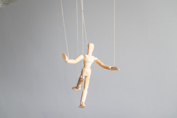 Human hand holds a wooden doll on the clothesline on a gray background. Power metaphor concept