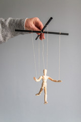 Human hand holds a wooden doll on the clothesline on a gray background. Power metaphor concept